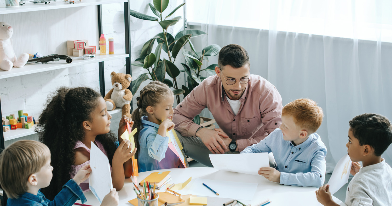 Foto von einem Erzieher mit einer Gruppe von Kindern an einem Tisch mit Malutensilien